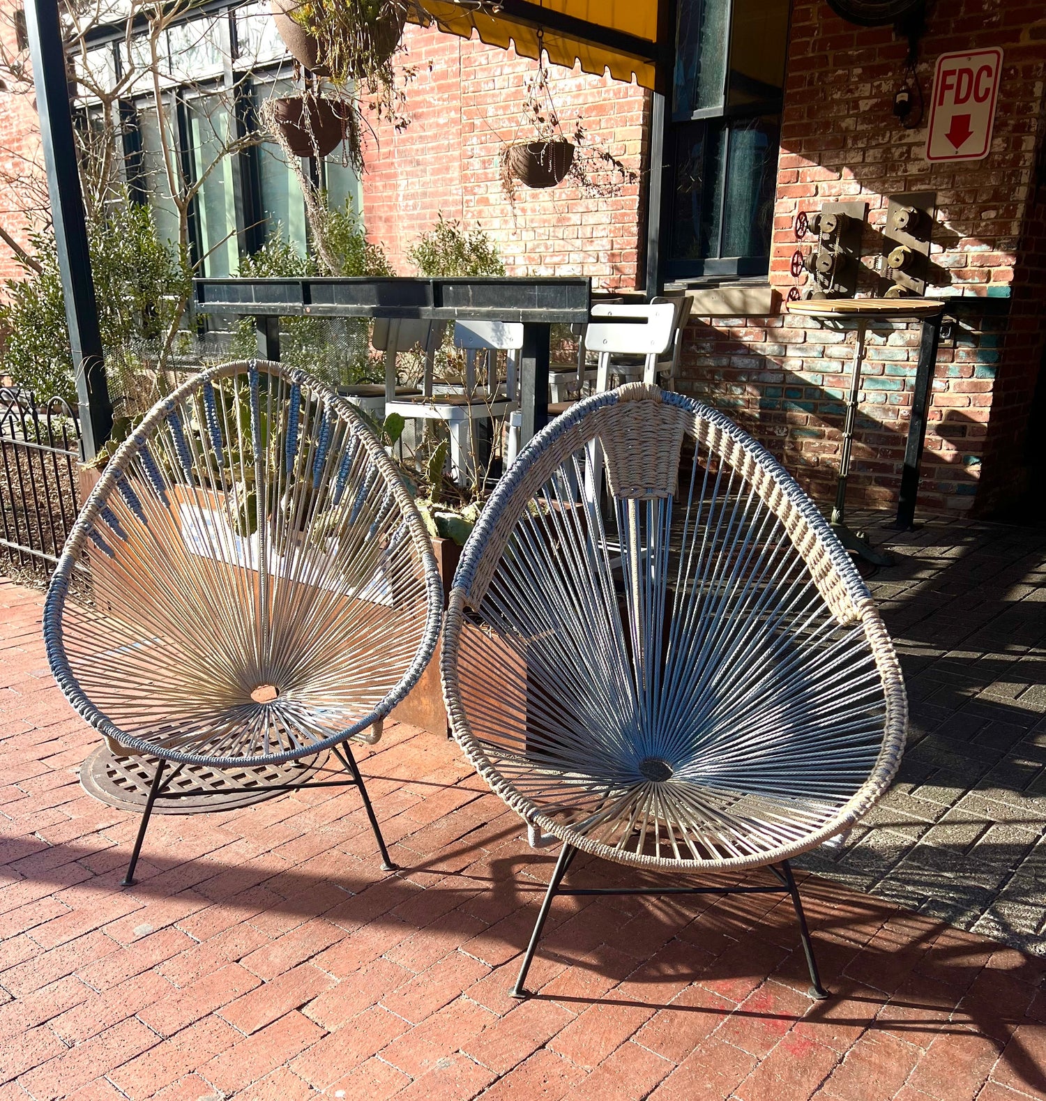 Two decorative outdoor chairs on a brick patio with a building in the background.
